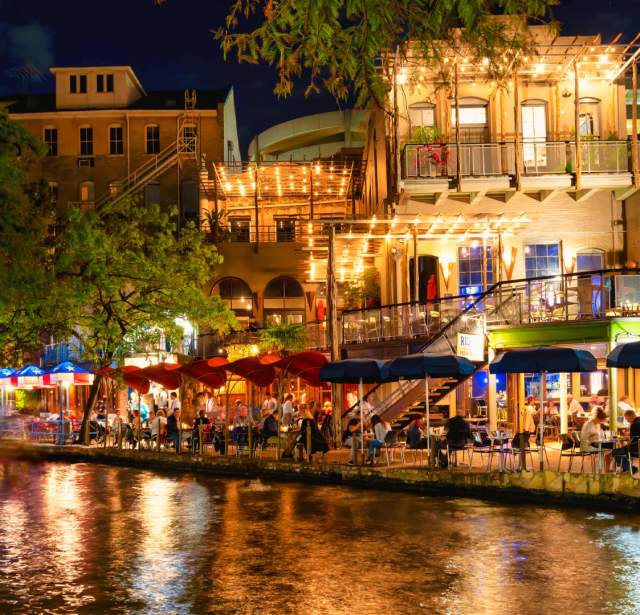 Restaurants along the River Walk in San Antonio at night with lights reflecting off the water.