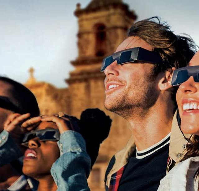 Group of friends in front of San Antonio Missions watching eclipse with protective eyewear