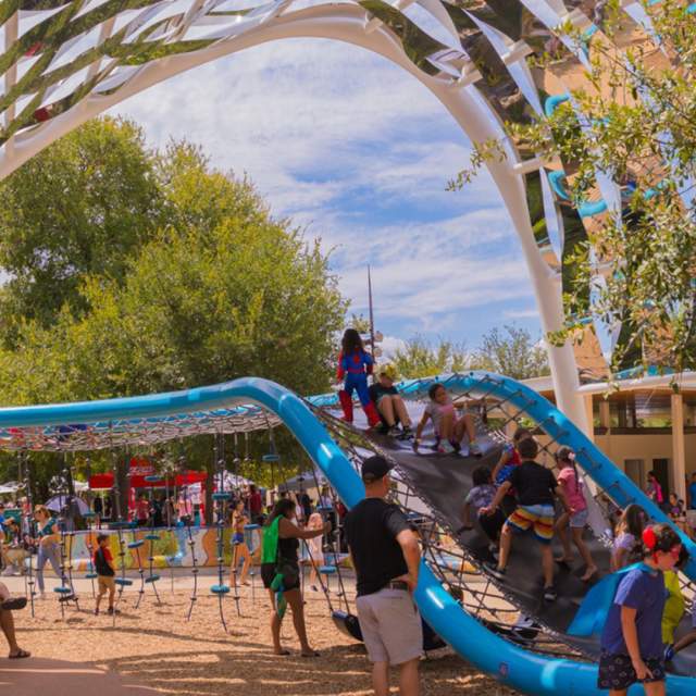 Children and families playing on outdoor blue play structure.