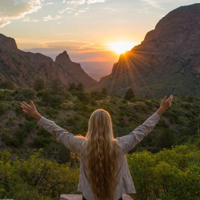 Girl with arms open overlooking sunset and valleys
