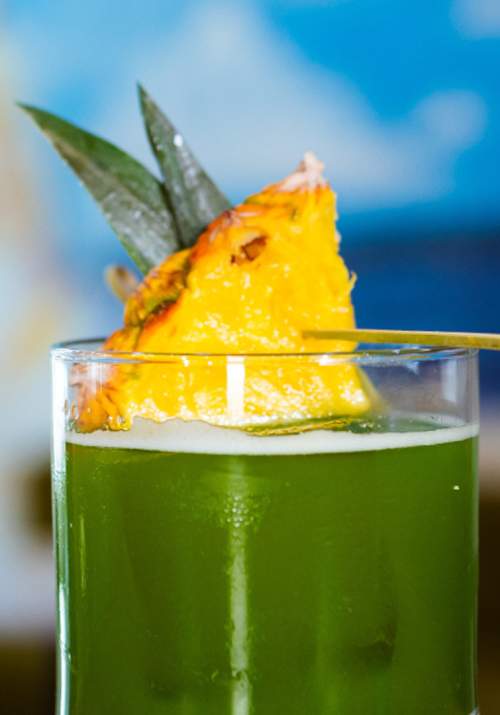 Green cocktail drink with pineapple on top.
