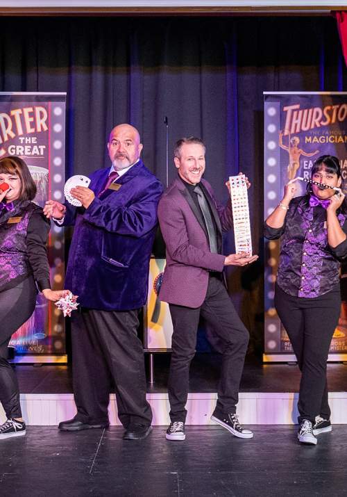 Magicians standing onstage in a row posing with various magician props.