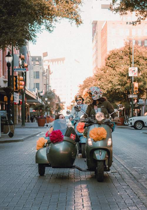 Woman driving vespa with passenger in side car in San Antonio, Texas.