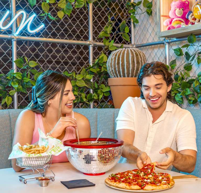 Boy and girl at table laughing, eating pizza, and enjoying drinks.