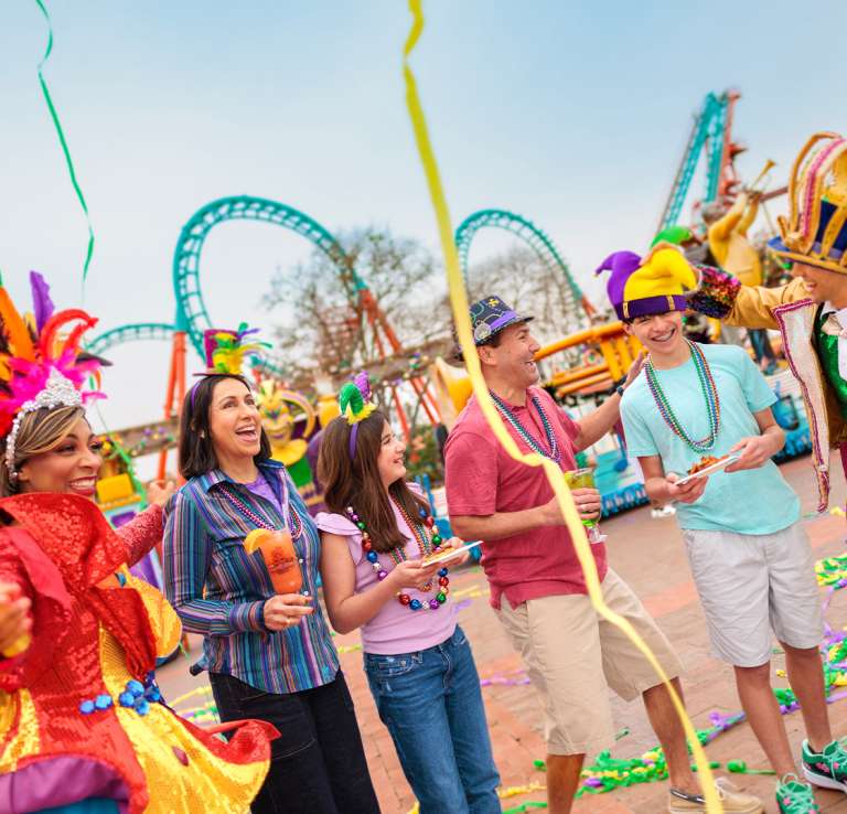 Family laughing with costumed characters at Six Flags Fiesta Texas Mardi Gras event.