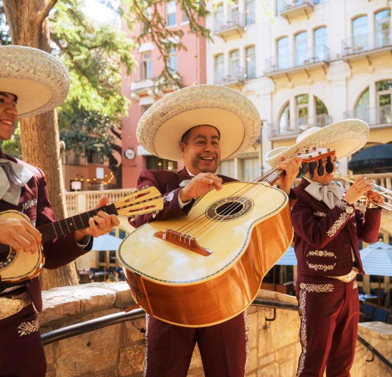A three-member mariachi band playing music on the River Walk.