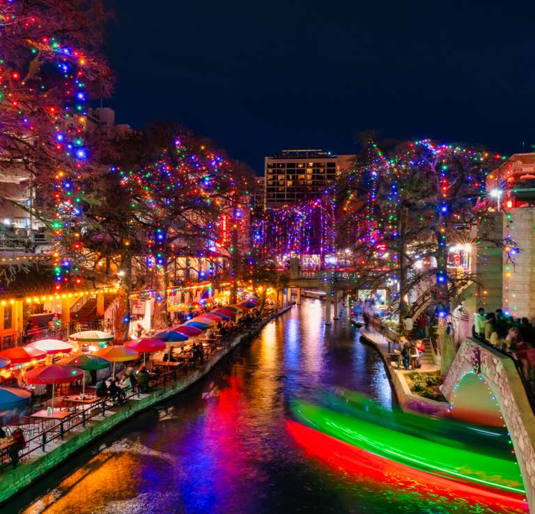 The San Antonio River Walk lit up at night with holiday lights.