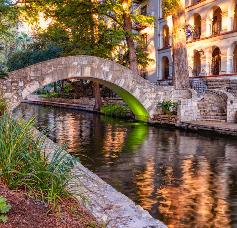Bridge at San Antonio River Walk with flowers and Omni La Mansion del Rio hotel in background.