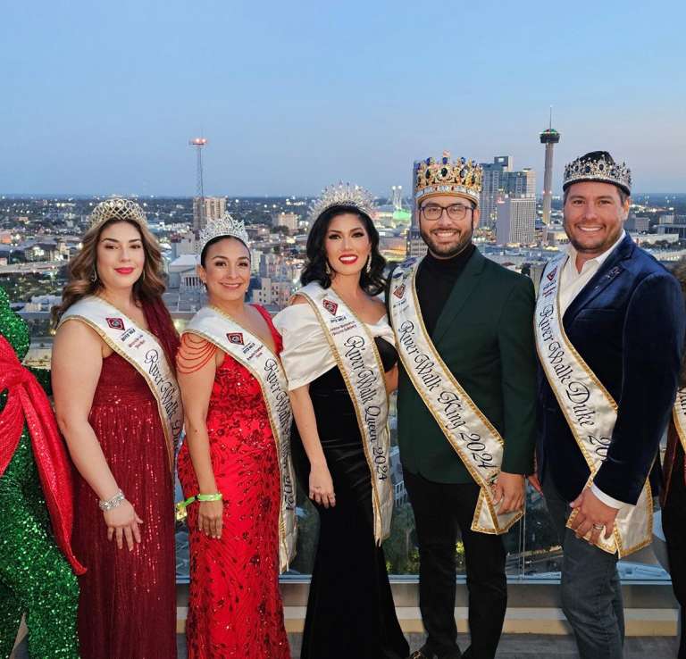 Group of people dressed in sashes and crowns with San Antonio skyline in background.