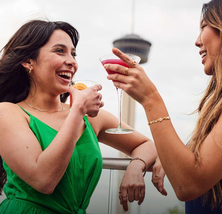 Two girls laughing and enjoying drinks with Tower of the Americas in background
