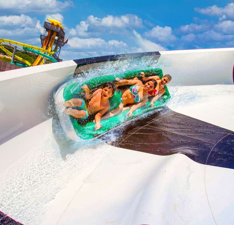 Group of three people on black and white water slide at Hurricane Harbor at Six Flags Fiesta Texas.