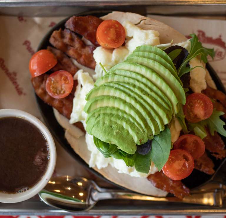 Overhead view of breakfst spreed with coffee and skillet with meal topped with avocado and tomatoes