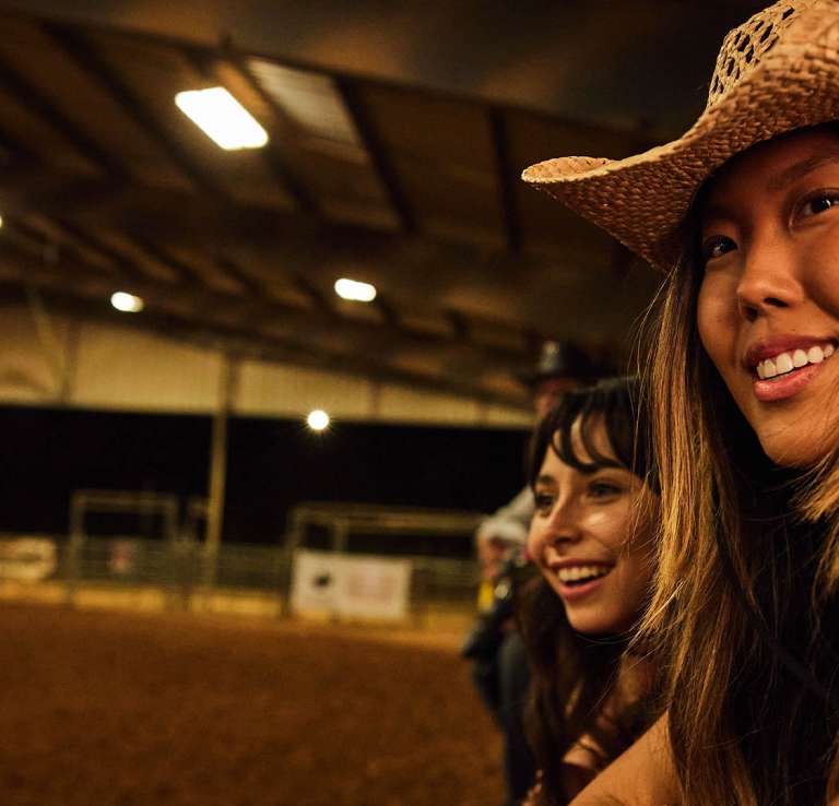 Gril in cowboy hat overlooking rodeo grounds.