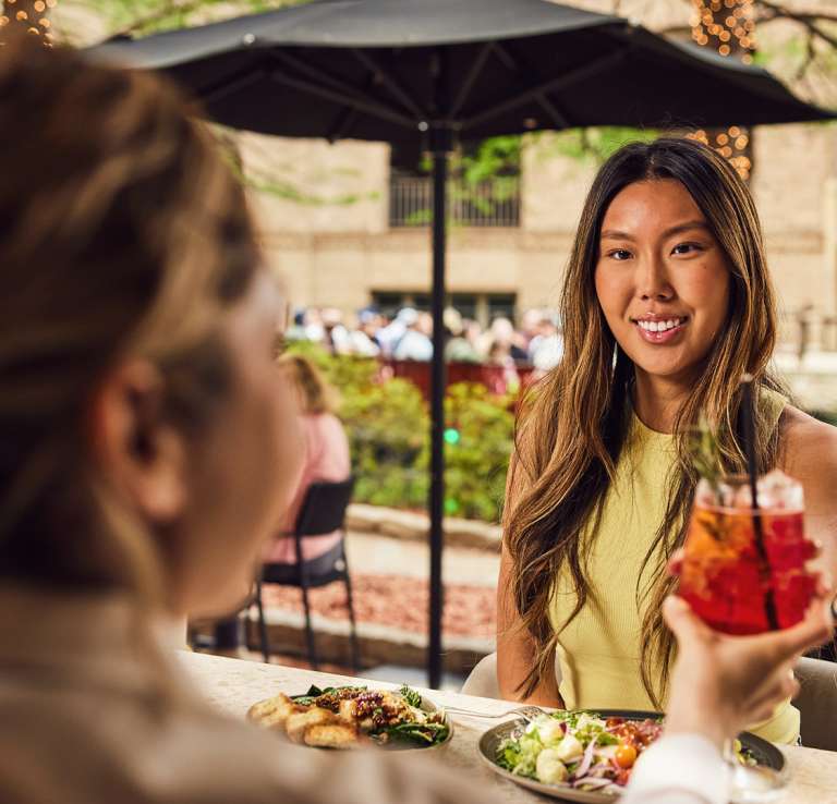 Woman accepting drink from waitress and smiling with San Antonio River Walk behind her.