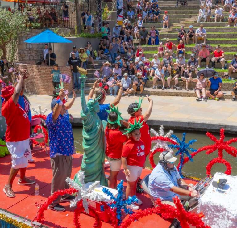 Patriotic group on river barge waving to crowd.
