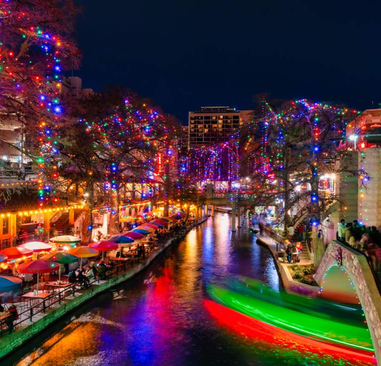 The San Antonio River Walk lit up at night with holiday lights.