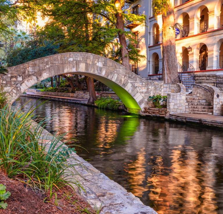 Bridge at San Antonio River Walk with flowers and Omni La Mansion del Rio hotel in background.