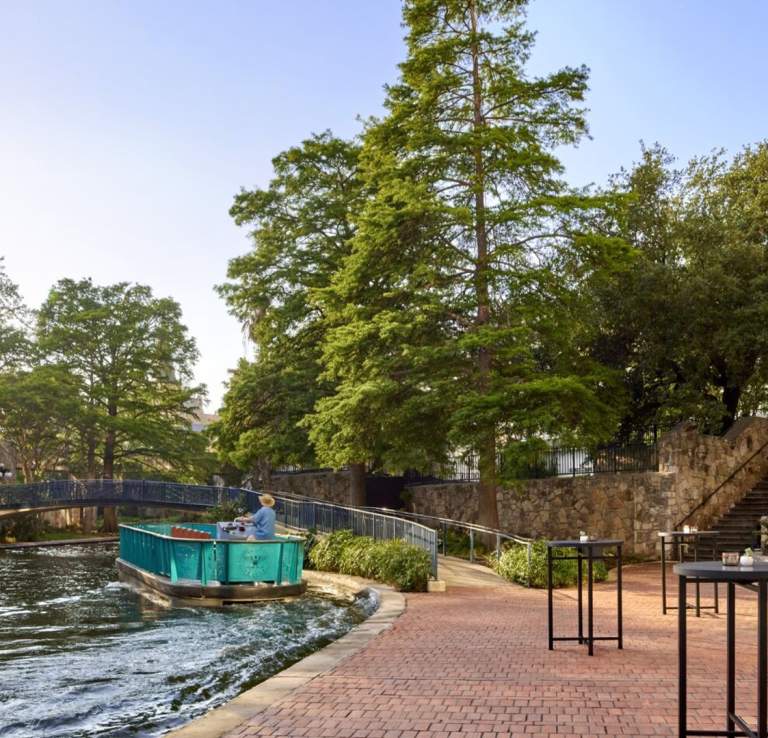 River barge floating along River Walk with large trees in background