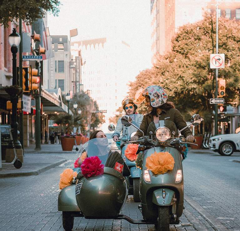 Woman driving vespa with passenger in side car in San Antonio, Texas.