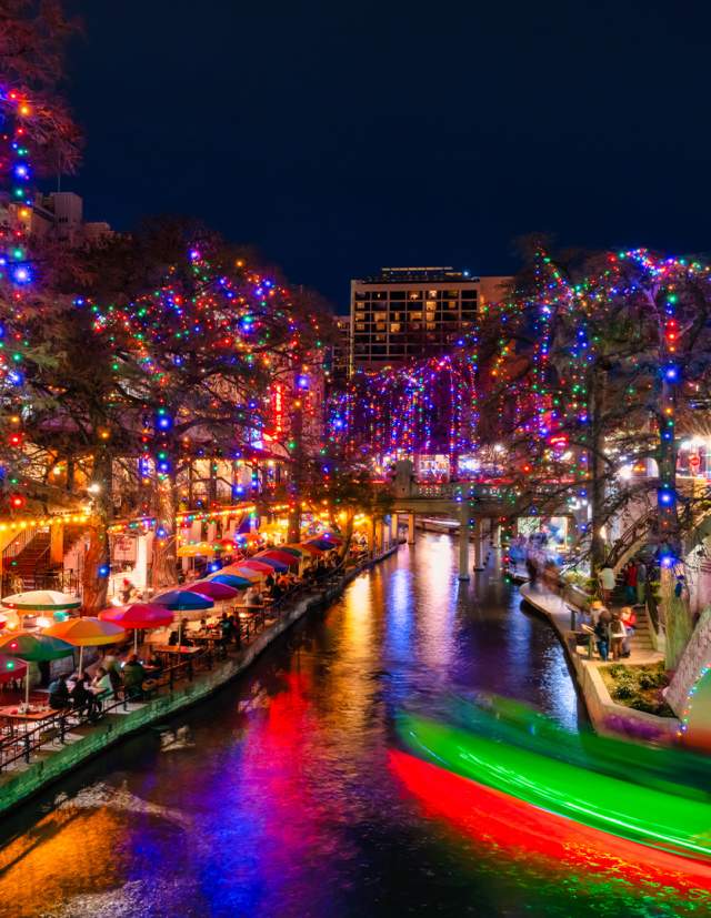 The San Antonio River Walk lit up at night with holiday lights.