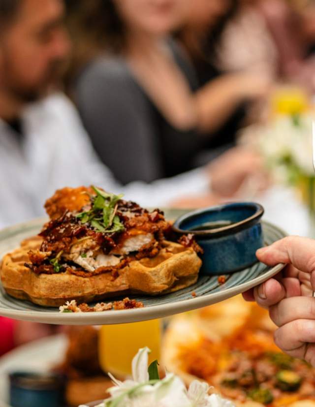 Hands passing eachother a plate of gourmet waffles.