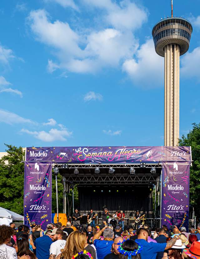 Crowd gathering in front of stage with Tower of the Americas in background.