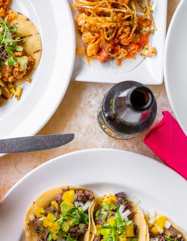 Overhead view of assorted taco plates, pink napkin, bottle, and iced tea at Acenar Restaurant.