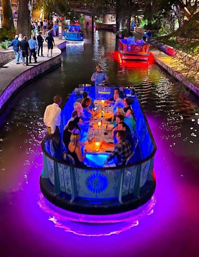 River Walk barge floating down river at night with purple glow underneath barge.
