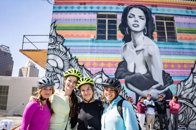 Group of girls wearing bike helmets in front of mural of woman
