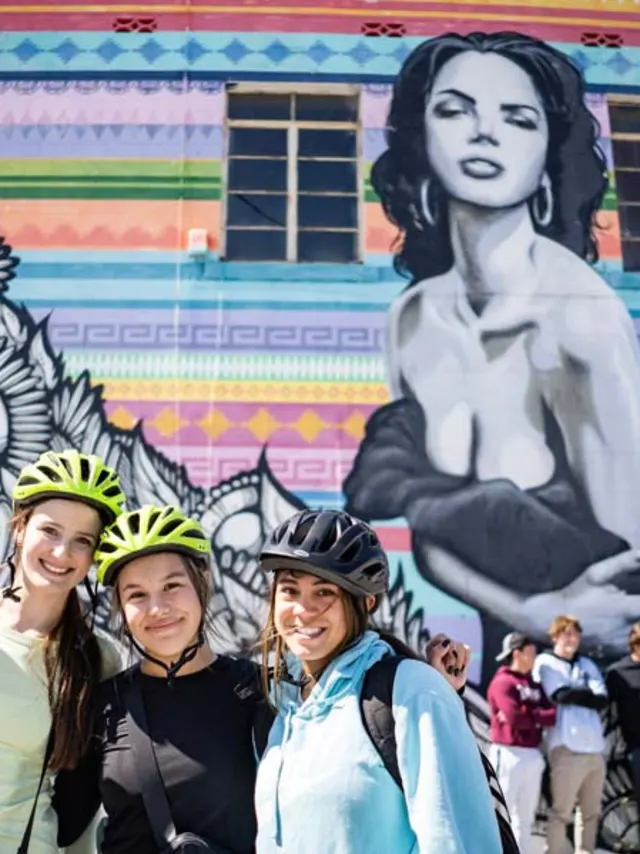 Group of girls wearing bike helmets in front of mural of woman