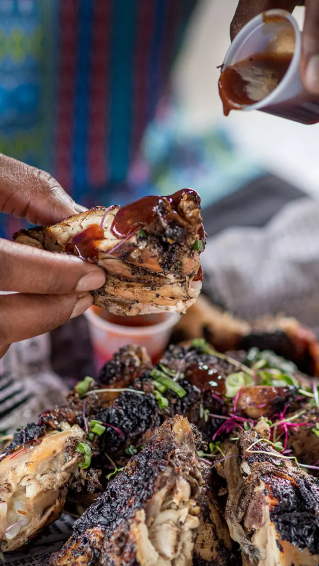 Hands dipping Jerk Chicken into barbecue sauce at The Jerk Shack.