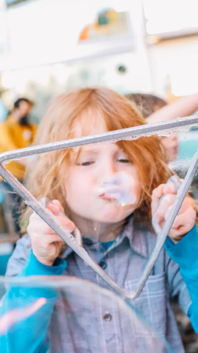 Child blowing bubble through triangular bubble-blower.