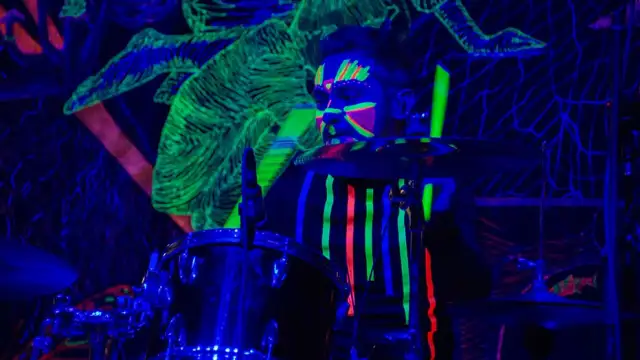 Man in glow-in-the-dark face paint playing drums under blacklight.