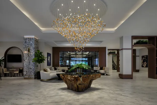 Modern hotel lobby with marble floors and a large chandelier above a wooden table