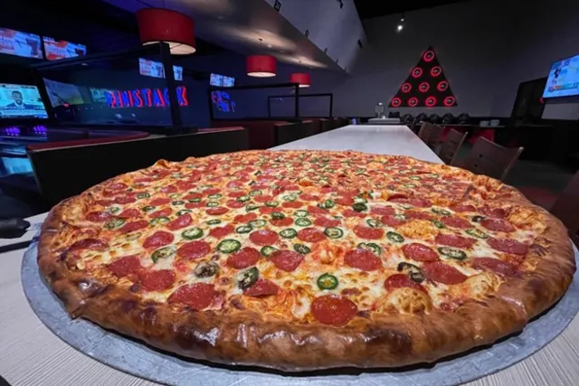 Extra-large pizza in front of bowling lanes at PINSTACK San Antonio.
