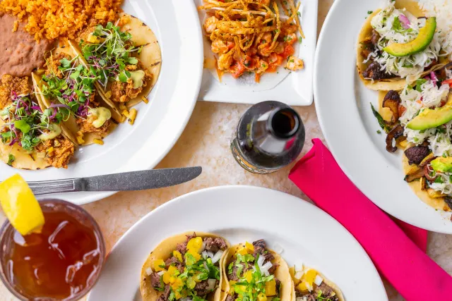 Overhead view of assorted taco plates, pink napkin, bottle, and iced tea at Acenar Restaurant.