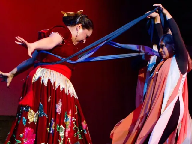 Two women in theatrical performances with cultural dresses and scarfs.