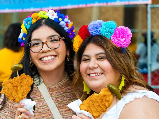Two girls holding chicken on a stick wearing flower crows at Fiesta San Antonio.