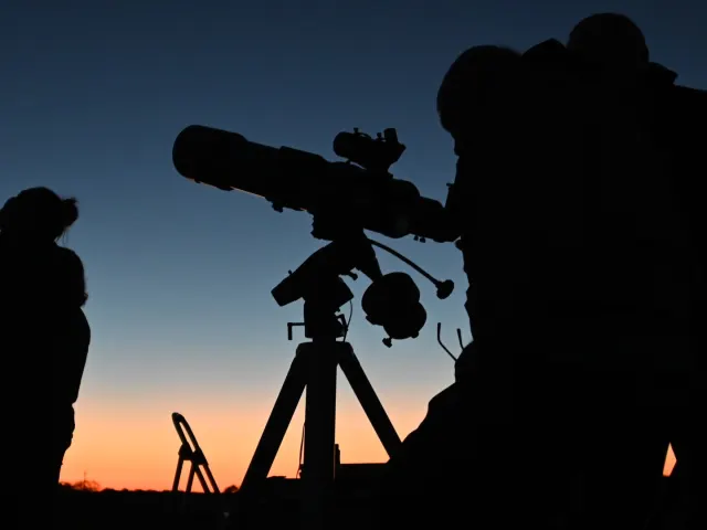 Silhouette of people looking through telescope