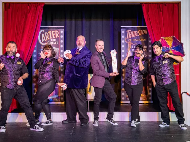 Magicians standing onstage in a row posing with various magician props.