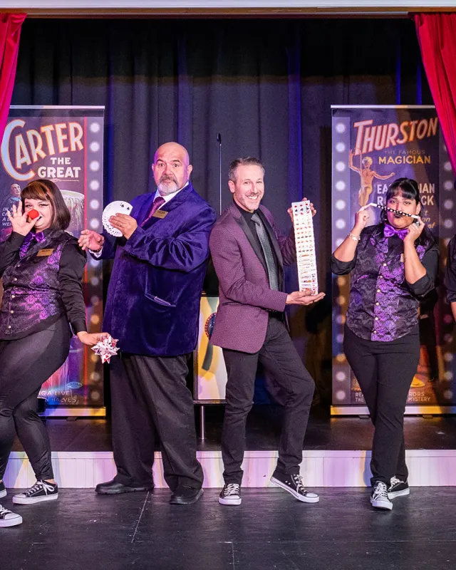 Magicians standing onstage in a row posing with various magician props.