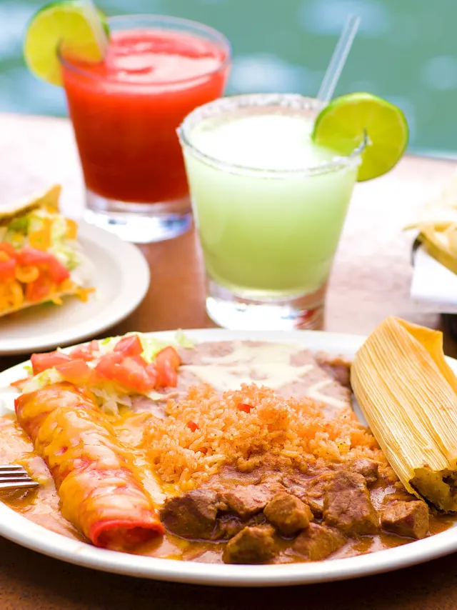 Plate of enchiladas, rice, and beans next to assorted side items and two margaritas at Casa Rio.