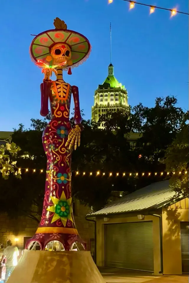 Large catrina statue in La Villita in San Antonio at dusk with a large building in the backround