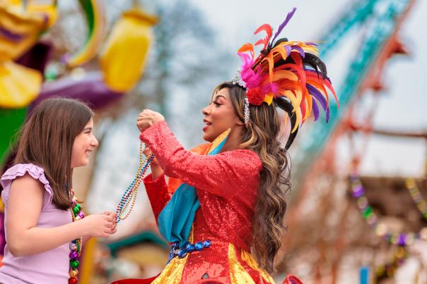 Costumed performer placing beads over girl's head at Six Flags Fiesta Texas' Mardi Gras Festival.