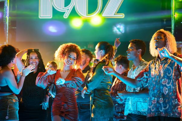 Group of people dancing at a 1902 nightclub with large "1902" sign above them.