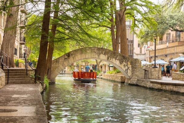 Red GO RIO River barge floating under bridge on San Antonio River Walk.