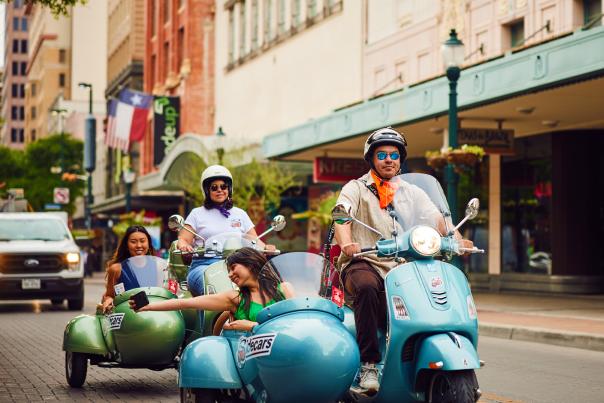 SiDECARS SA Vespa with driver and rider cruising in San Antonio.