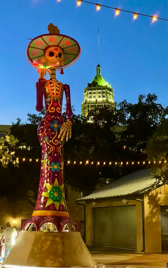 Large catrina statue in La Villita in San Antonio at dusk with a large building in the backround