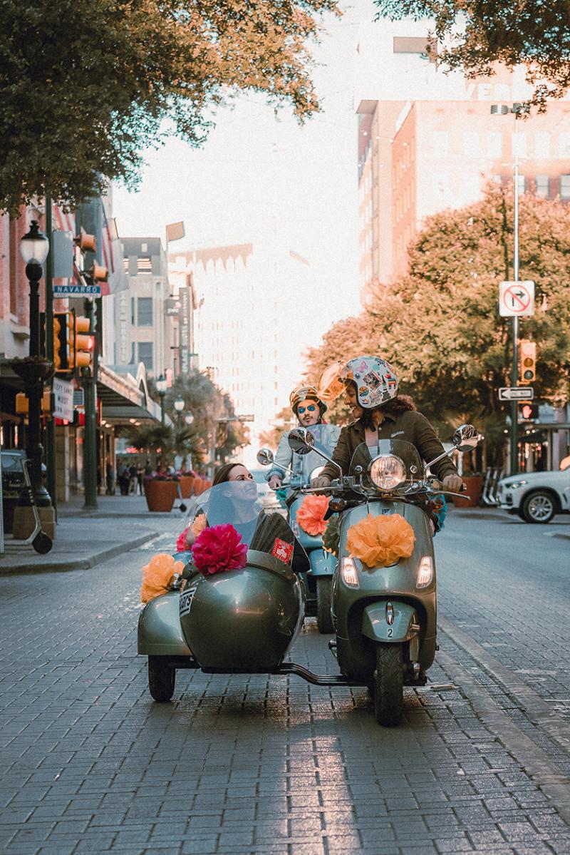 Woman driving vespa with passenger in side car in San Antonio, Texas.
