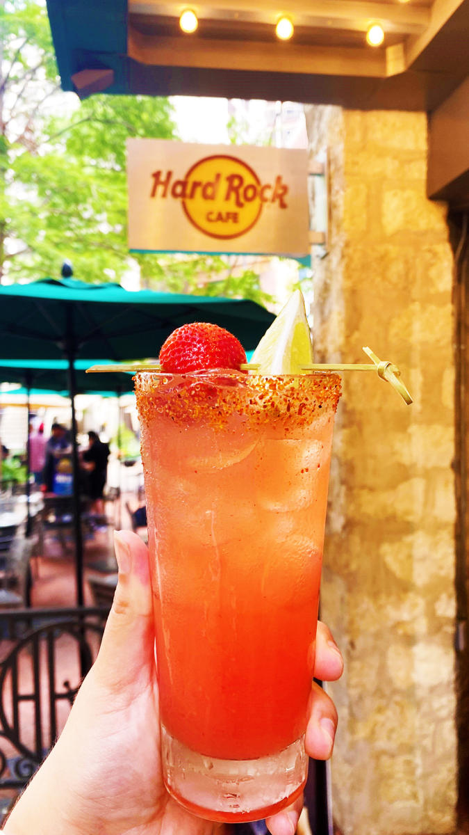 Cocktail held in front of Hard Rock Cafe sign with strawberry.